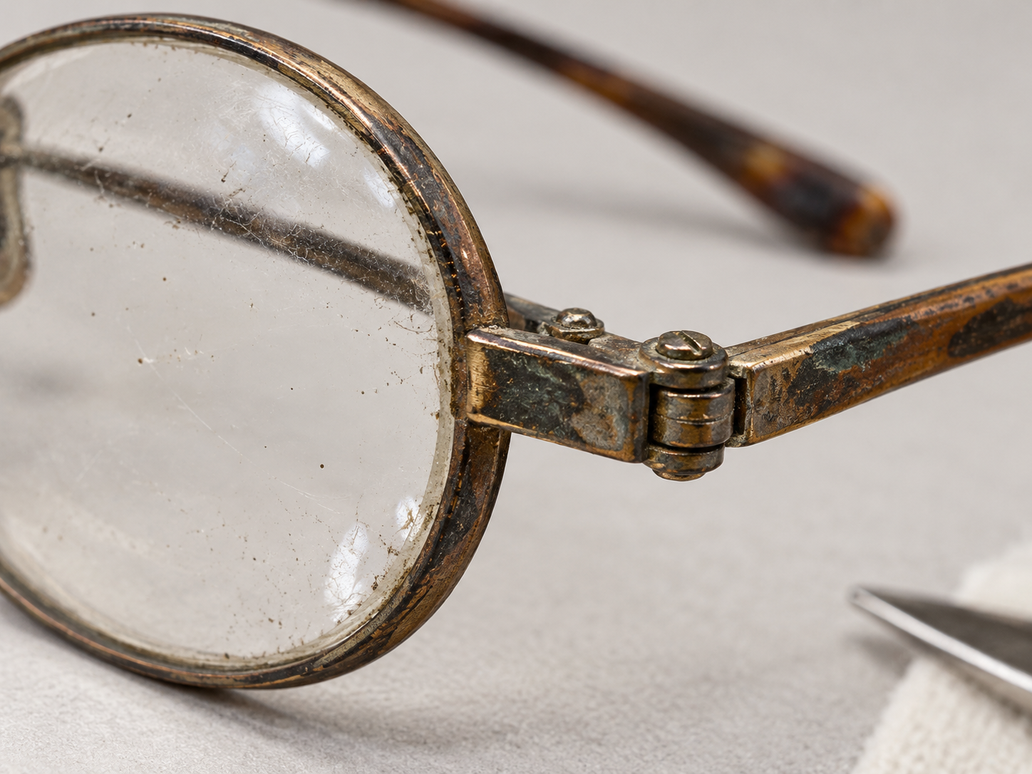 Interpretative editorial close-up of the hinge of an aged pair of eyeglasses, showing patina and construction detail.